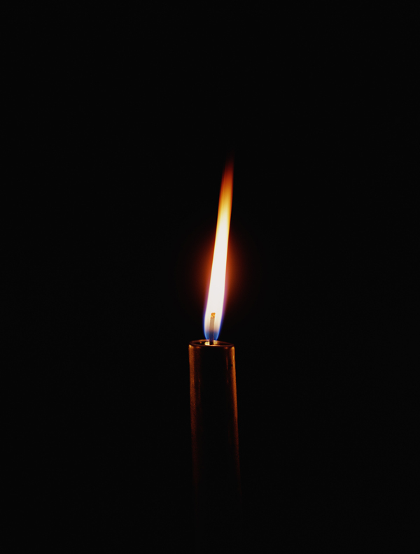 A single lit candle burning against total darkness.