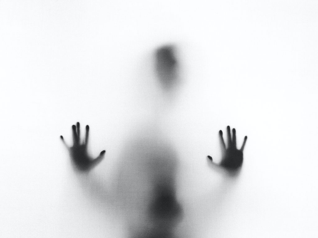 A person's silhouette with hands pressed against frosted glass.