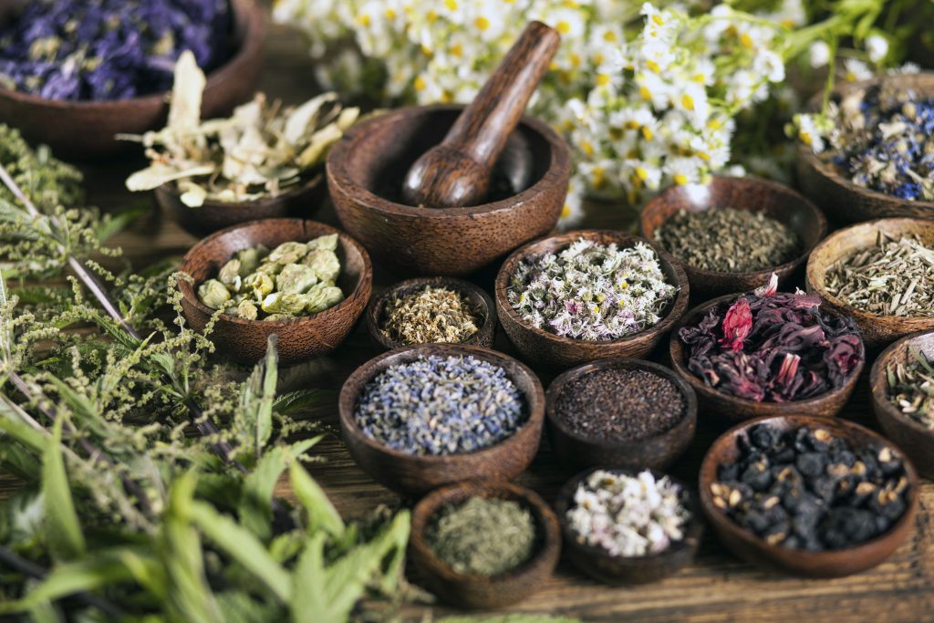 Small wooden bowls of dried herbs, flowers, and spices arranged around a mortar and pestle.